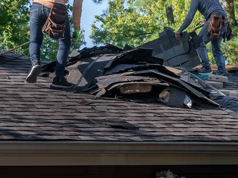 Two roofers removing old shingles from a residential roof in order to get the roof ready for a replacement
